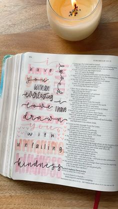 an open bible next to a candle on top of a wooden table with writing in it