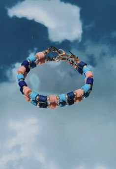 a blue and pink beaded bracelet hanging from a hook on a cloudy sky background