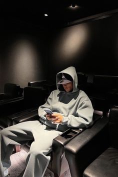 a man in a hoodie is sitting on a couch and looking at his cell phone