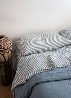 a bed with blue and white striped comforter next to a vase on the floor