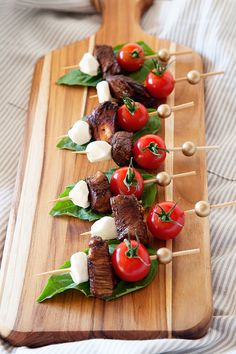 several skewered meats with tomatoes and cheese on a wooden board, ready to be served