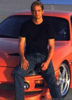 a man sitting on the hood of an orange sports car with his feet propped up