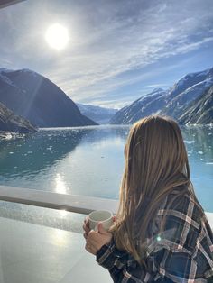 a woman holding a cup looking out over the water