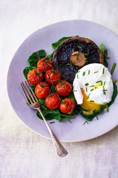 a white plate topped with an egg, tomatoes and spinach covered in sauce next to a fork