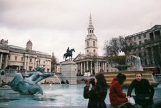 some people are sitting near a fountain with a horse statue in the background and buildings