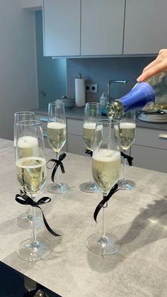 a person pouring champagne into wine glasses on a kitchen counter with black ribbon around them