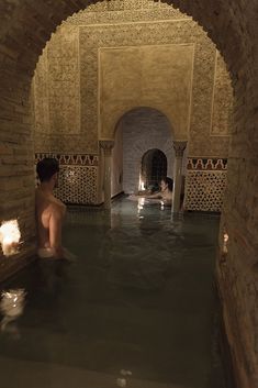 a person sitting in a bathtub with candles on the floor and water running through it