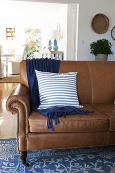 a brown leather couch with blue and white throw pillows on top of it, sitting in a living room