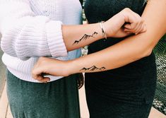 two women with matching tattoos on their arms and armbands, both holding each other's hands