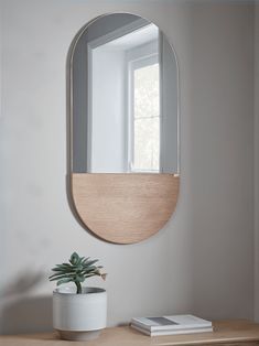 a round mirror sitting on top of a wooden table next to a potted plant