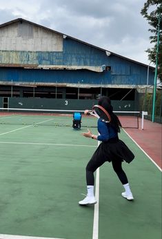 a woman is playing tennis on an outdoor court in front of a blue and green building