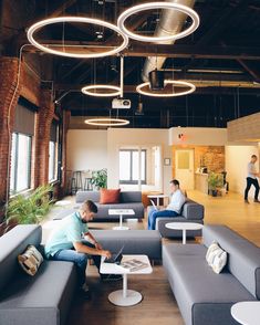 two men are sitting on couches in an open space with exposed ceilings and large windows