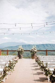 an outdoor ceremony set up with white chairs and greenery on the aisle, surrounded by string lights