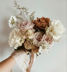 a person holding a bouquet of flowers in their hand with the background white and gray