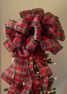 a red and green plaid bow on top of a christmas tree with lights around it