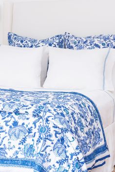 a white bed with blue and white bedspread on it's headboard