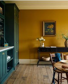 a dining room with yellow walls and wooden flooring is pictured in this image, there are two vases on the table