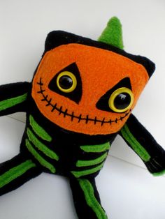 an orange and black stuffed animal wearing a green halloween costume with big eyes, sitting on top of a white surface