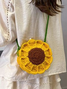 a woman wearing a white shirt holding a yellow and brown crocheted sunflower purse