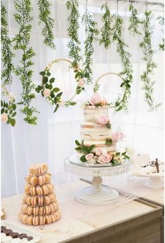 a wedding cake with flowers and greenery hanging from the ceiling next to macaroons