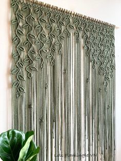 a green plant sitting on top of a wooden table next to a wall hanging with tassels