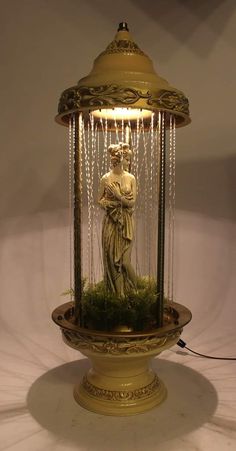 a statue in a glass container with chains hanging from it's sides and a light on top