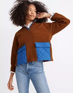 a woman in a brown and blue sweater poses for the camera with her hands on her head