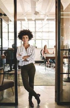 a woman standing in an office doorway with her arms crossed and looking at the camera