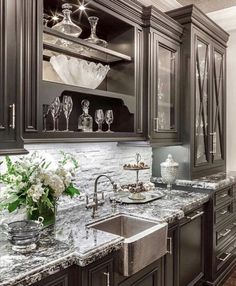 a kitchen with marble counter tops and dark wood cabinets, white flowers in vases on the sink