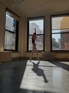 a ballerina is standing in front of three large windows and stretching her arms up