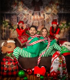 a man and woman sitting on a couch in front of christmas decorations with santa's helpers