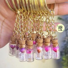 a hand holding a bunch of tiny glass bottles filled with pink liquid and gold chains