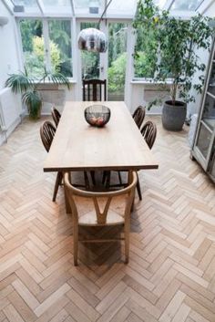 a dining table and chairs in a room with large windows on both sides, surrounded by wood parquet flooring