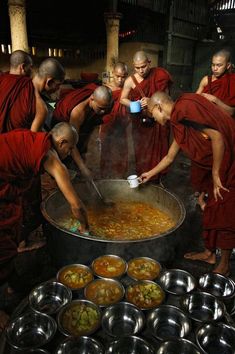 monks are gathered around a large pot filled with food and water, as one man pours something into the bowl