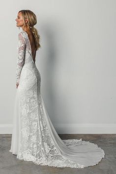 a woman in a wedding dress standing against a wall with her back to the camera