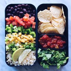 two black trays filled with different types of food on top of a white table