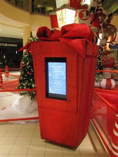 a large red box with a screen on it in the middle of a shopping mall