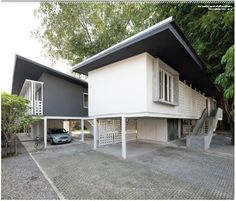 two cars are parked in front of a house with white walls and black roofing