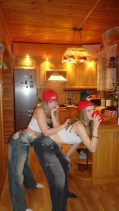 two young women in jeans and red bandanas drinking from cups while standing on the kitchen floor