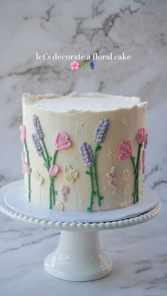 a white cake with pink and purple flowers on it sitting on top of a plate