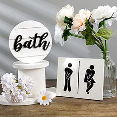 a vase filled with white flowers next to bathroom signs