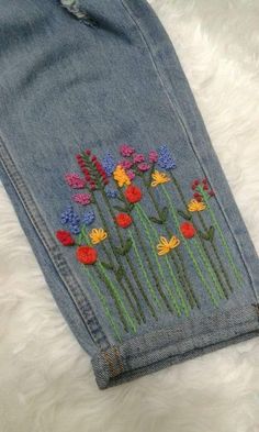 a pair of jeans with flowers embroidered on the front and back, sitting on a white furnishing