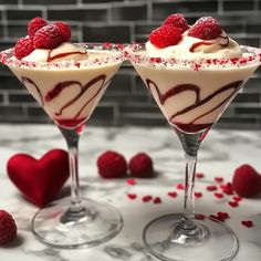 two martinis with raspberries and whipped cream in them on a marble table