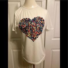 White Crew-Neck Short-Sleeved Tee With Bold Multi-Colored Heart Graphic. 65% Cotton/35% Polyester. White Heart-shaped T-shirt For Spring, Casual V-neck Top With Heart Print, White Short Sleeve T-shirt With Heart Print, Red Heart Graphic Top For Spring, White Heart Print T-shirt For Summer, Red Tops With Heart Graphic For Spring, Multicolor Heart Print Crew Neck Top, White Heart Print T-shirt For Spring, Casual White Tops With Heart Graphic