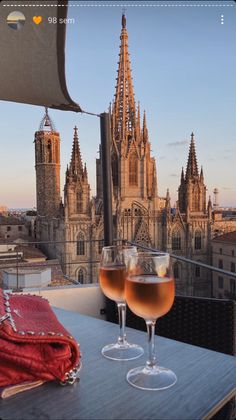 two glasses of wine sitting on top of a wooden table next to a tall building