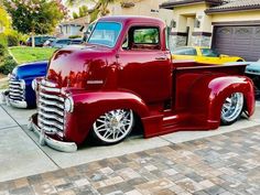 an old red truck parked in front of a yellow and blue car on a driveway