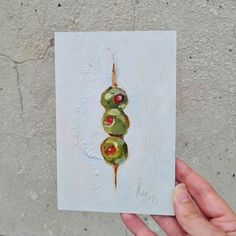 a hand holding up a piece of art that looks like a caterpillar on white paper