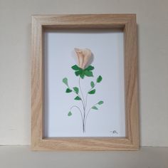 a white flower with green leaves is in a wooden frame on the wall next to a shelf