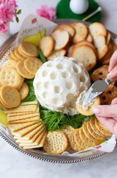 a platter with crackers, cheese ball and golf chips on it is being held by someone's hand