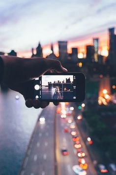 a person holding up a cell phone to take a photo of the city at night